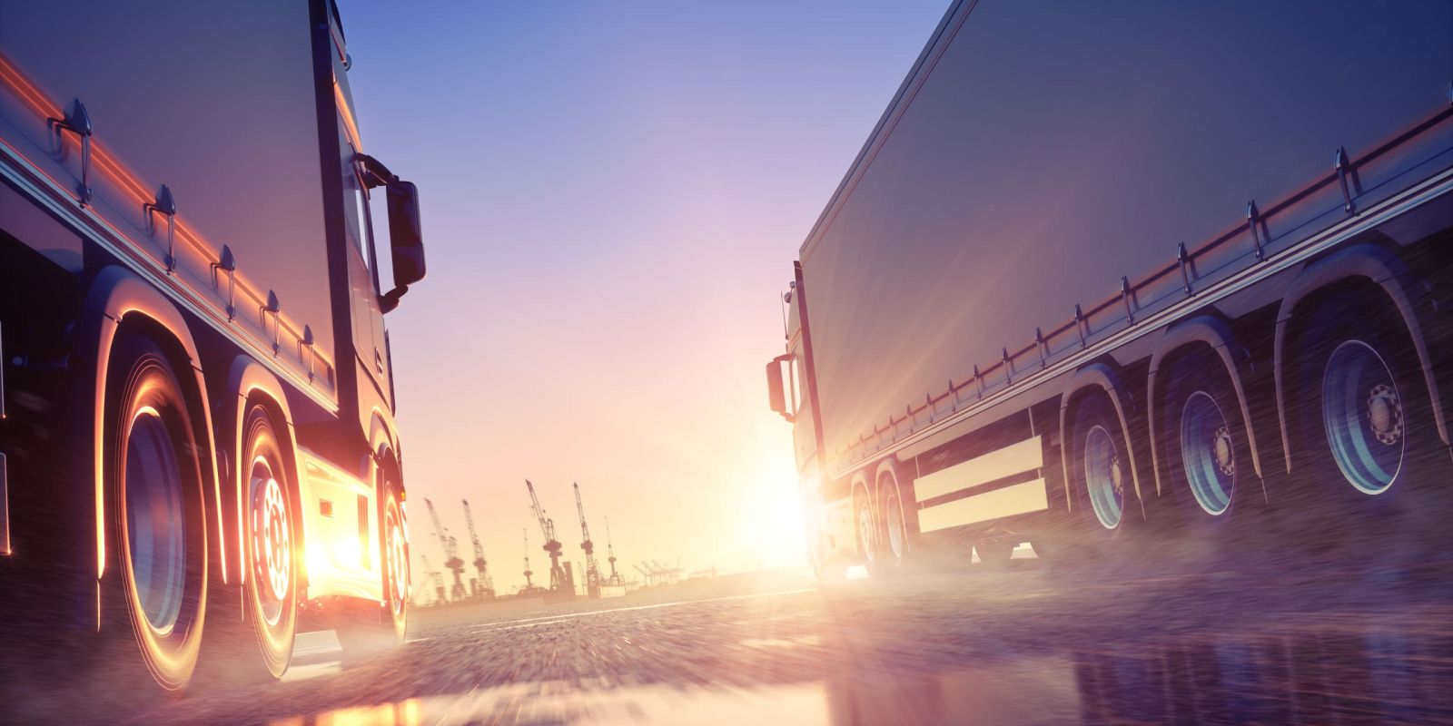 Zwei LKWs vor Hafen, zwischen Ihnen geht die Sonne auf